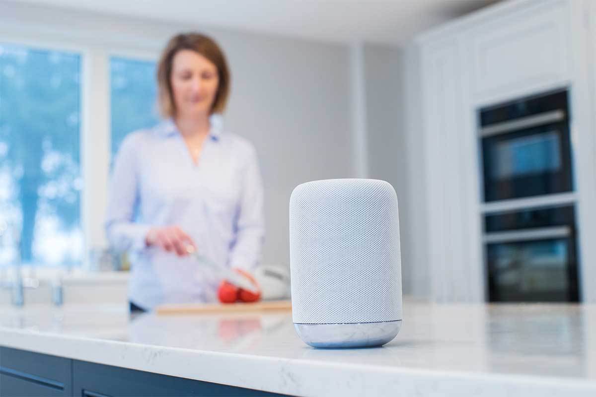 Close-up of a smart speaker with a woman cooking in the background