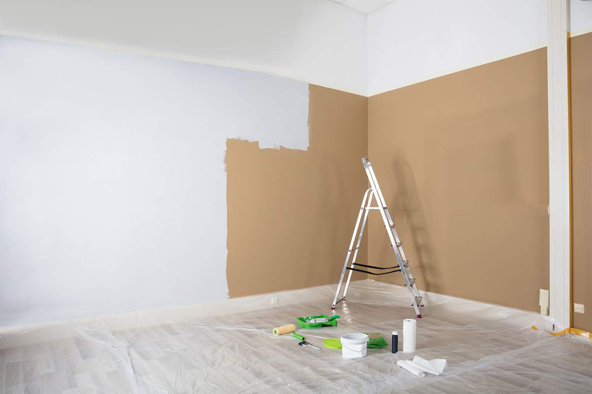 Room half painted white with ladder and painting tools