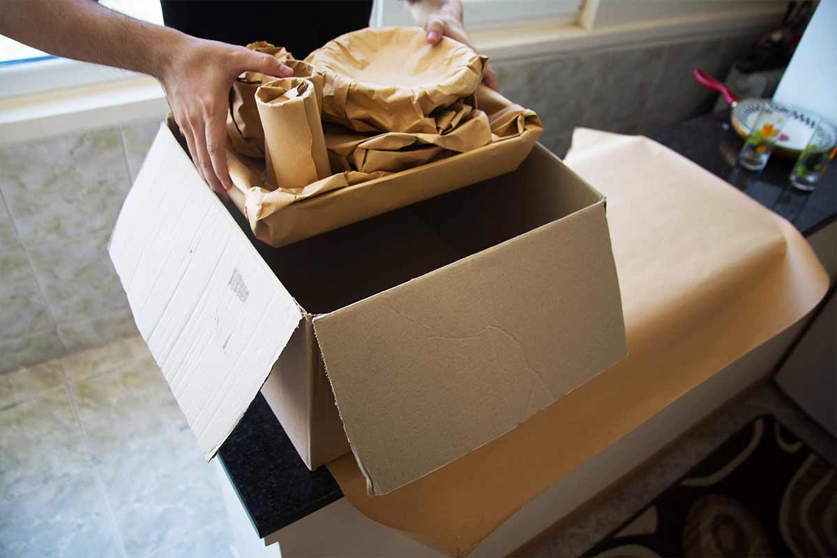 man packing dishware wrapped in moving paper