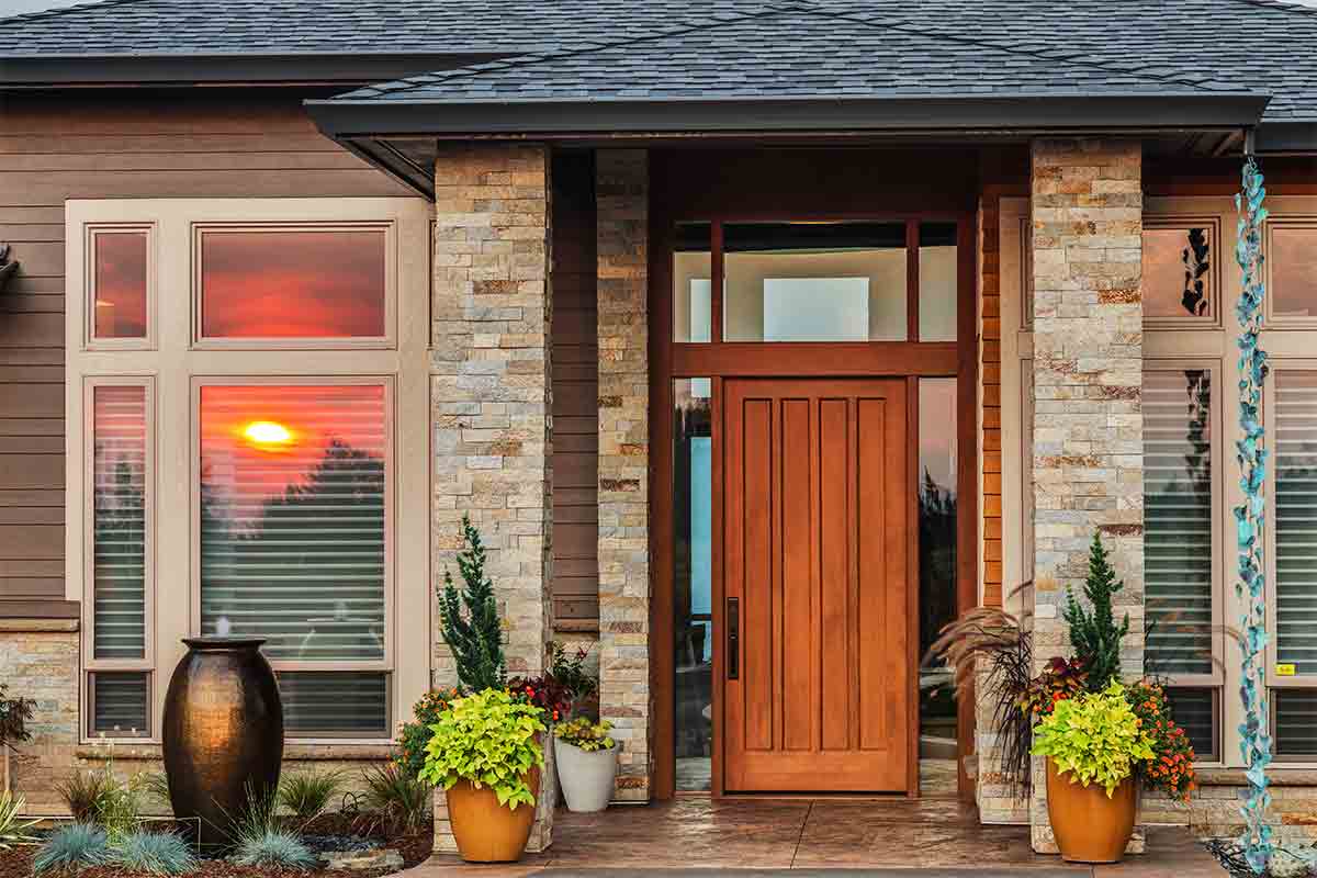 Wooden front entry door on a modern-style house with sunset reflected in front window of house