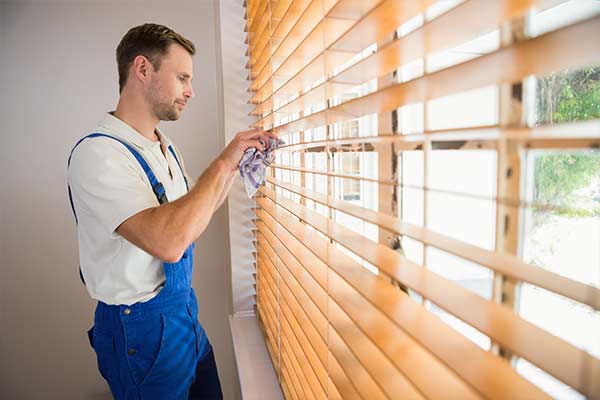 man cleaning window blinds with a rag