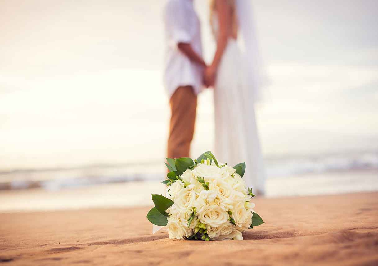 couple kissing behind wedding bouquet on the beach