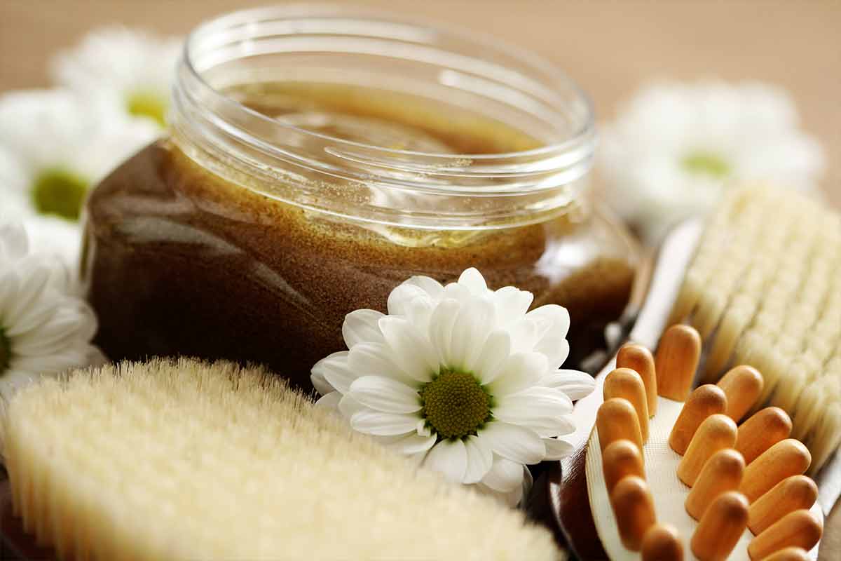 body scrub in jar surrounded by flowers and brushes