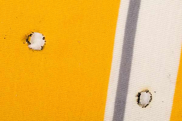 cigarette burn holes on yellow and white fabric