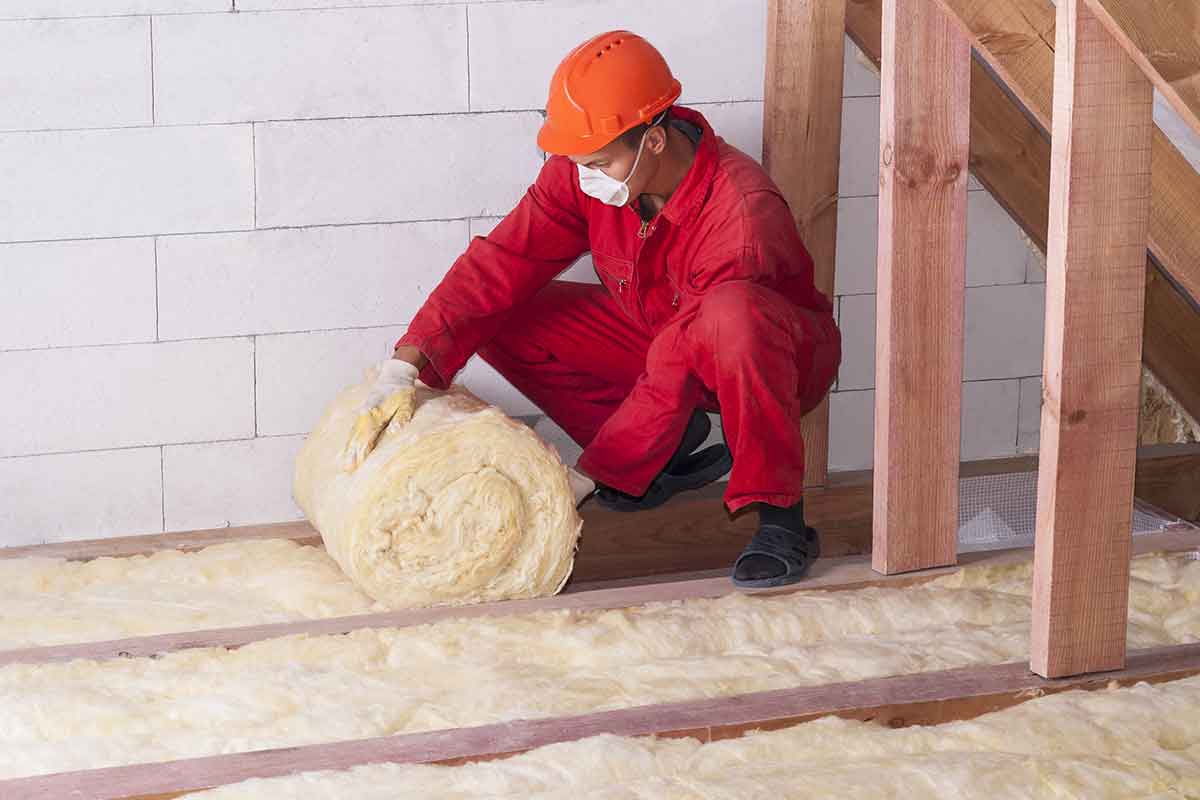 man installs fiberglass insulation in attic