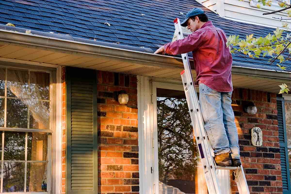 man standing on ladder while cleaning gutters