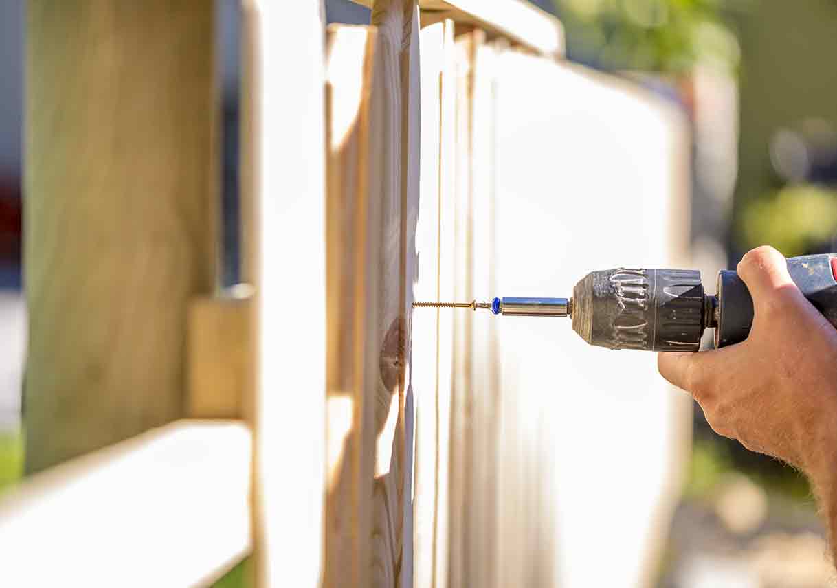 man erecting wood fence with drill