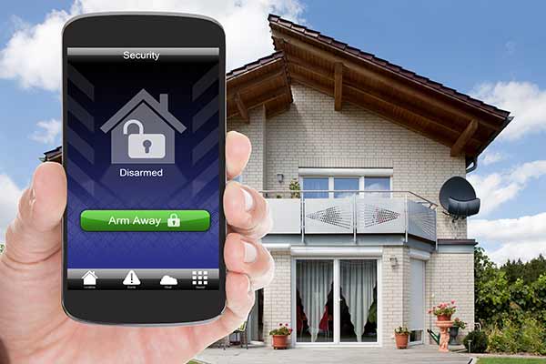 hand holding cell phone showing remote home alarm system with modern home in background