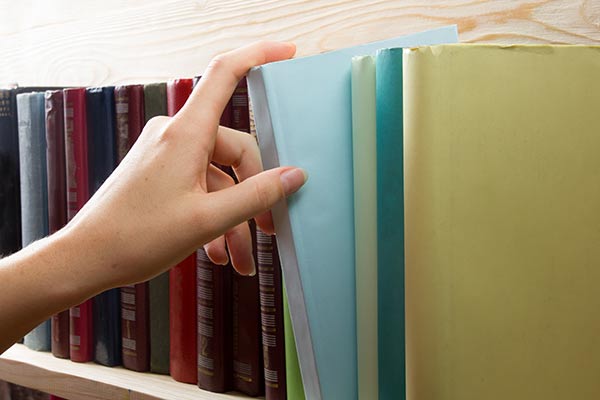 woman's hand pulling book off the shelf