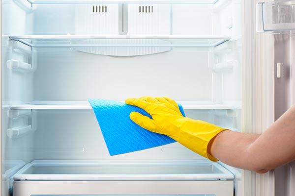 yellow gloved hand wipes down empty fridge with rag