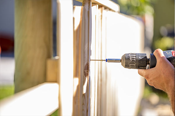 man working on a wooden fence with a drill