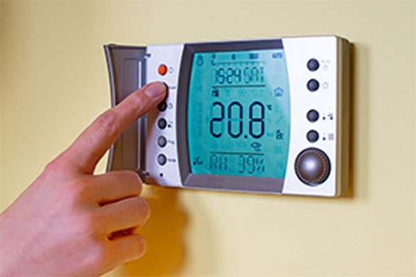 woman's hand changing modern wall mounted programmable thermostat